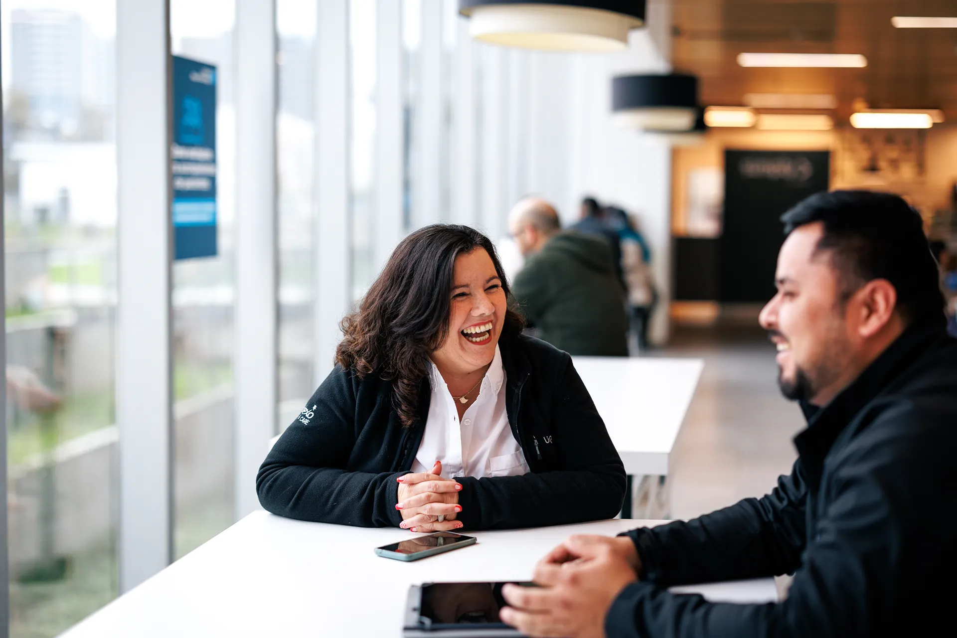 Two colleagues laughing together at a table in a bright office